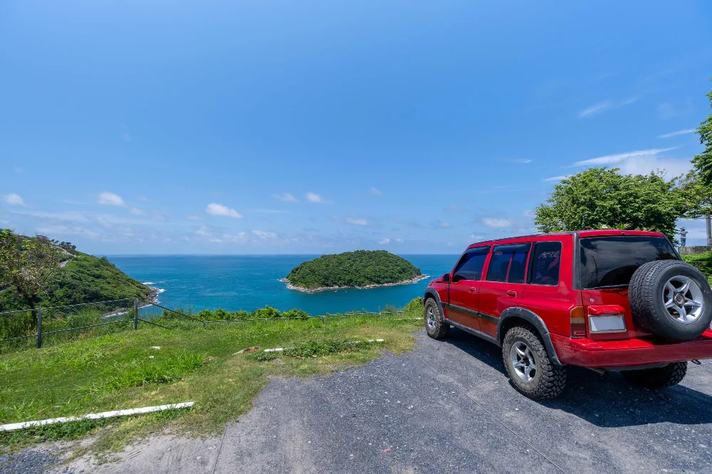 Auto a noleggio 4x4 rossa parcheggiata su una strada costiera con vista su una piccola isola delle Bahamas